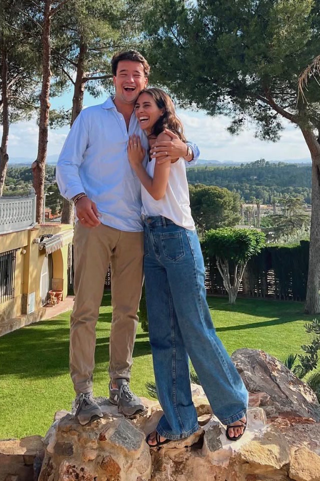 Quique Mira y María Lorenzo abrazados y riendo en un jardín con pinos